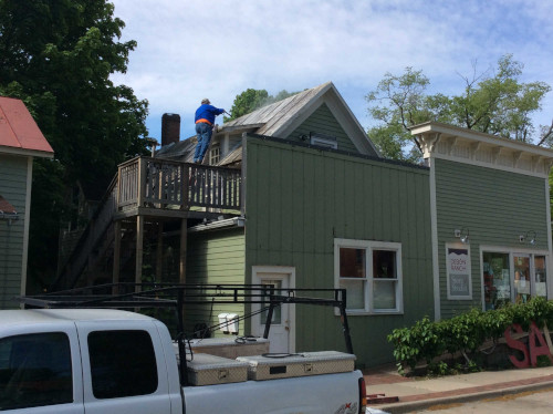 A photo of Scott using a scraper on a pole to finish cleaning the metal roof.