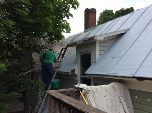 Photo of Scott working on priming the metal roof under an overhanging tree.