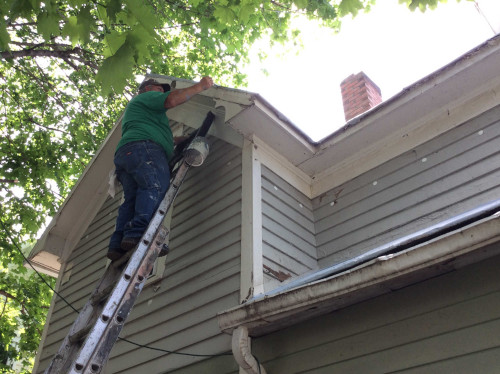 Photo of Scott on a ladder, priming the edge of the roof with a small paintbrush.